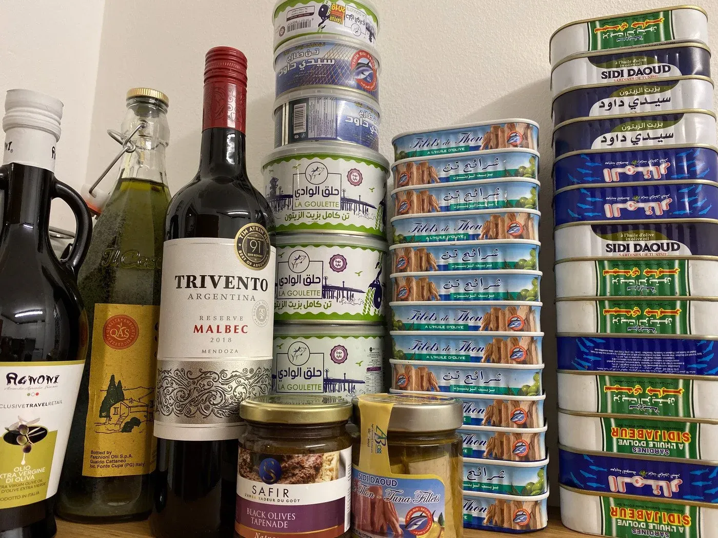 A stack of Tunisian sardine tins next to wine and olive oil